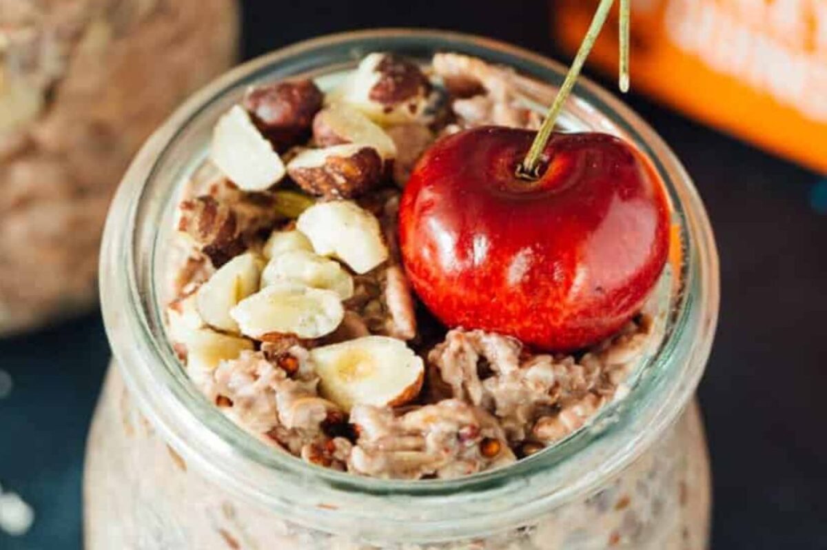 A glass jar filled with oatmeal topped with chopped nuts and a whole cherry on top, perfect for those exploring cherry recipes.
