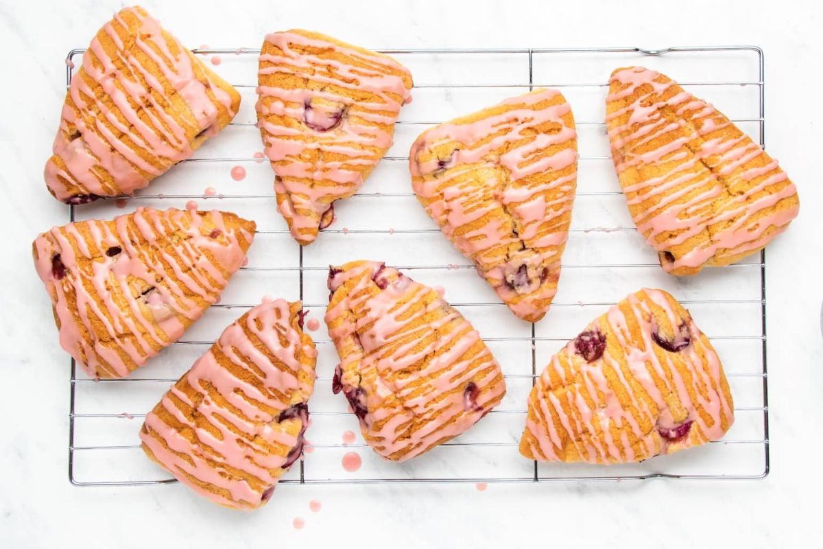 Eight triangular pastries with pink drizzle icing, each inspired by cherry recipes, placed on a wire cooling rack.