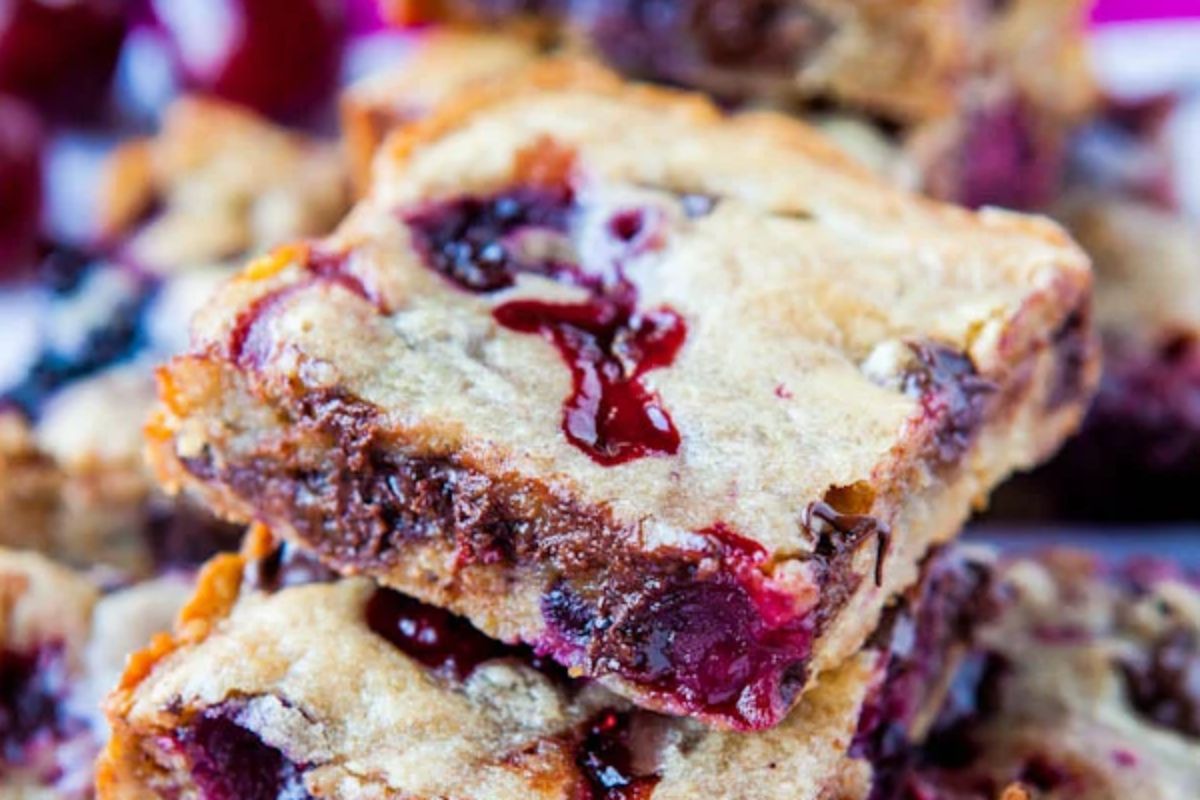 Close-up of a stack of cherry chocolate bars, showcasing a golden-brown crust with visible cherries and melted chocolate—a tempting treat perfect for any cherry recipe collection.