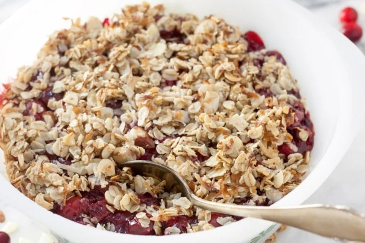 A bowl of freshly baked cherry crumble with oat and nut topping, served with a spoon.