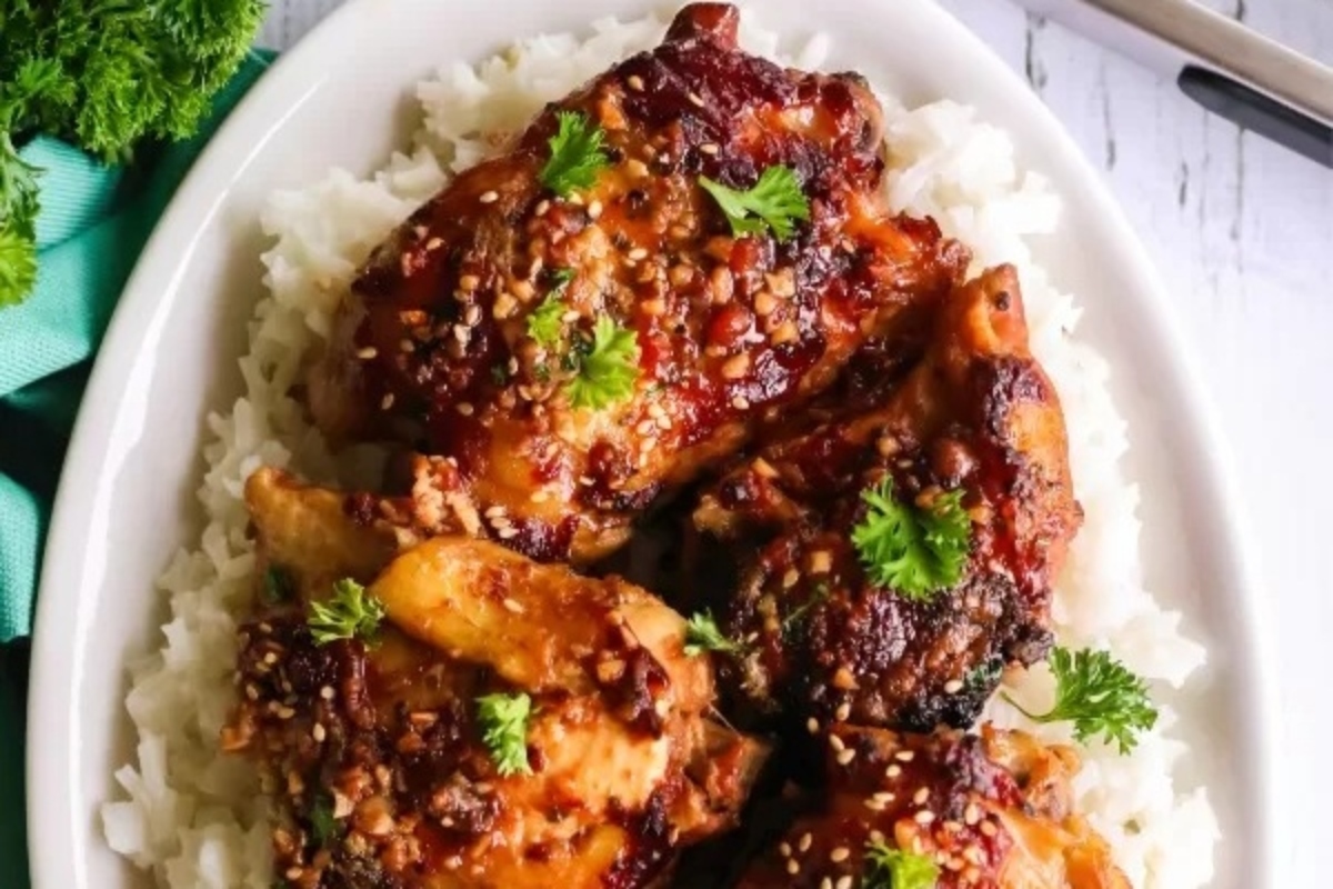 A plate of white rice topped with four pieces of cooked chicken thighs, garnished with parsley and sesame seeds. Perfect for those searching for delicious chicken thigh recipes.