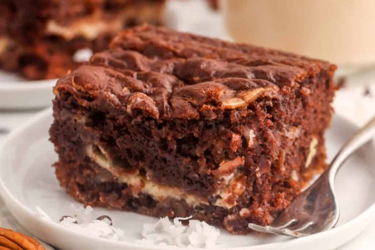 A delightful piece of layered chocolate and cream dessert sits invitingly on a white plate with a fork, showcasing one of the best shortcut desserts you can easily prepare at home.