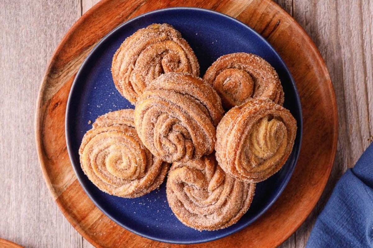 A blue plate on a wooden board holds six cinnamon sugar pastries arranged in a circular pattern, showcasing perfect shortcut desserts for any occasion.