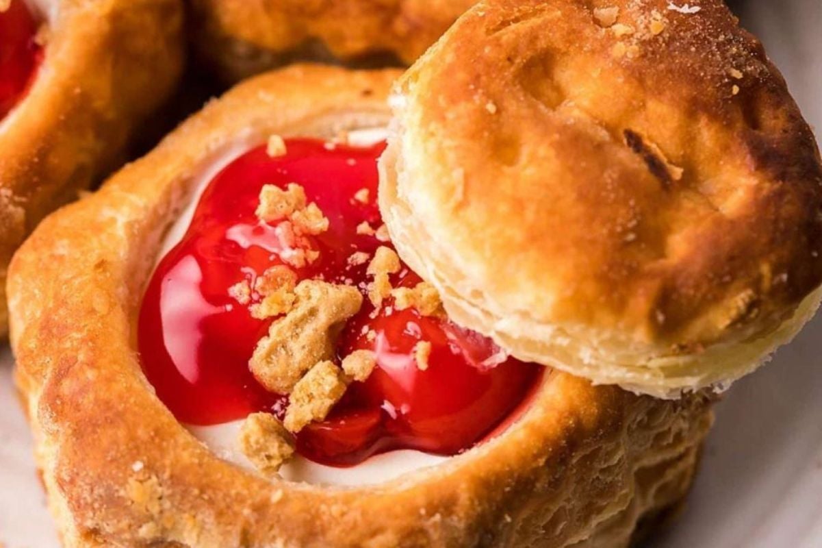 Close-up of an easy dessert: a golden-brown pastry filled with creamy white frosting, topped with bright red cherry filling and crumbled biscuit pieces.