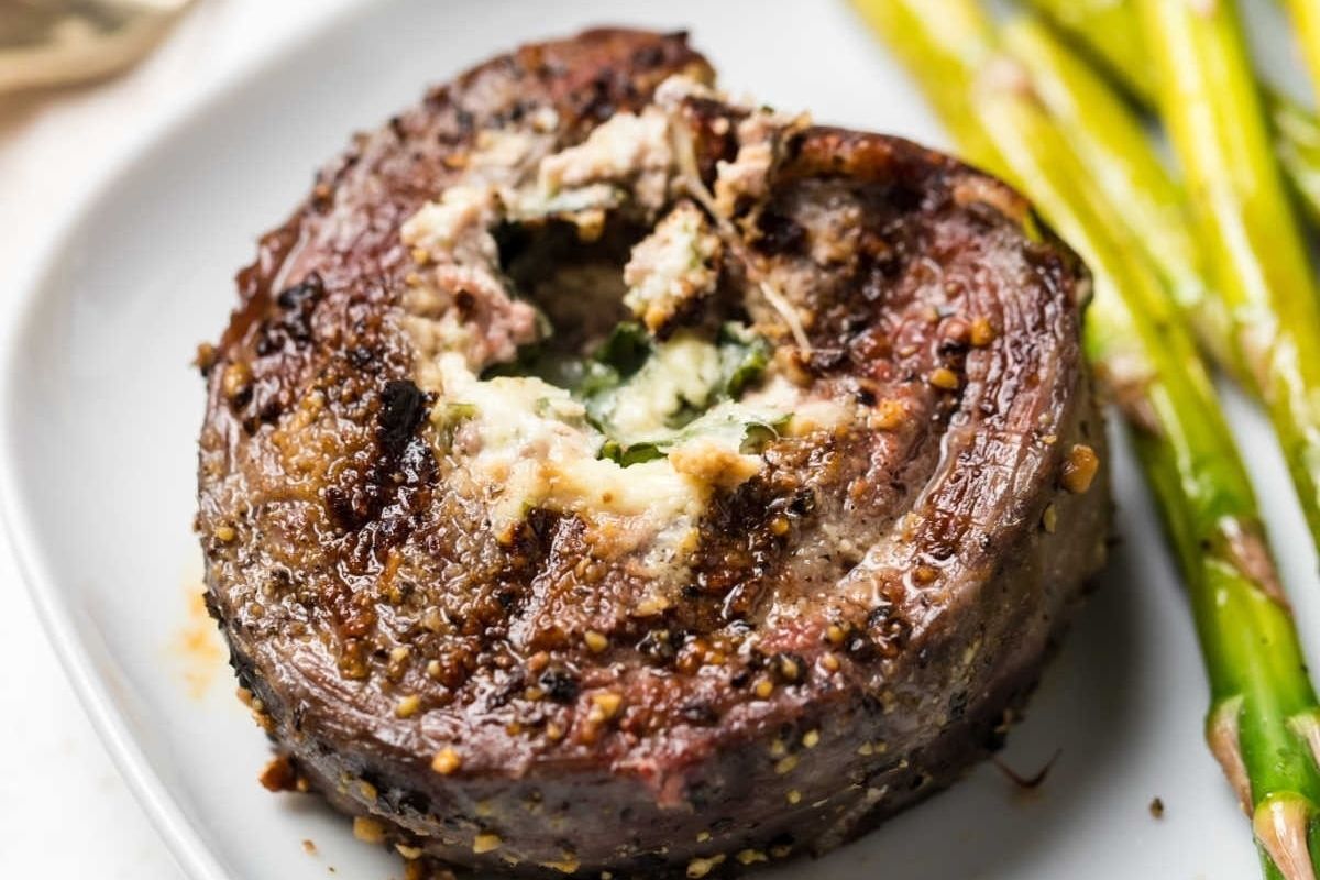 Grilled flank steak recipes seasoned with spices and topped with a dollop of melted butter, served next to asparagus spears on a white plate.