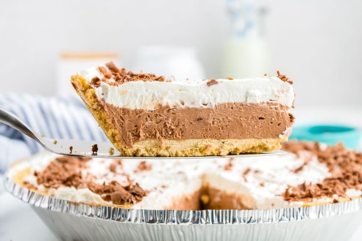 A slice of layered chocolate cream pie with a crumbly crust is held up with a serving utensil above the remainder of this easy dessert pie.
