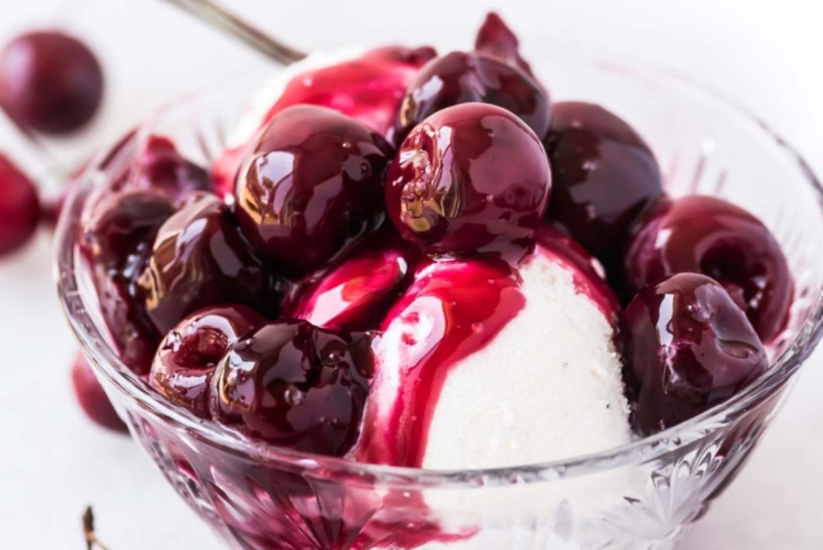 A glass bowl of vanilla ice cream topped with whole cherries and drizzled with cherry syrup, making it one of the most delightful cherry recipes.