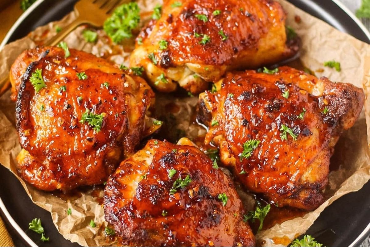 A plate with four pieces of roasted chicken thighs garnished with parsley, served on parchment paper—one of our tastiest chicken thigh recipes.