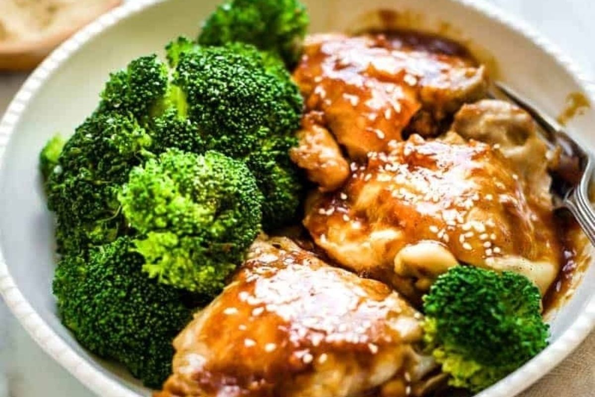 A plate of cooked broccoli and glazed chicken thigh pieces garnished with sesame seeds.