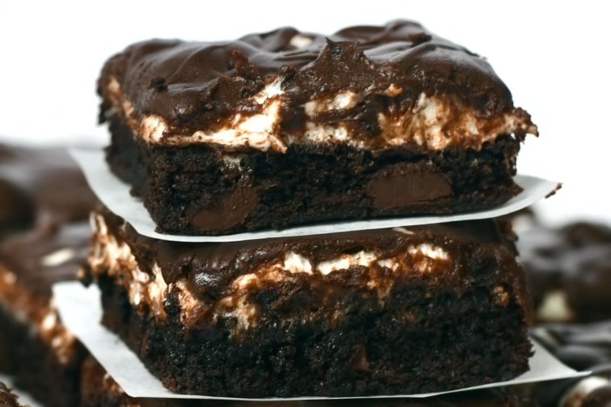 Two fudgy chocolate brownies stacked on top of each other, featuring visible chunks of chocolate and a layer of creamy marshmallow. These shortcut desserts are placed on parchment paper.