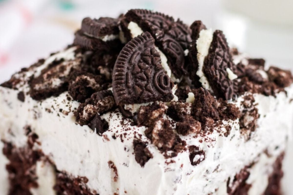 A close-up of a dessert topped with crushed chocolate cookies and whipped cream on a chocolate cake base.