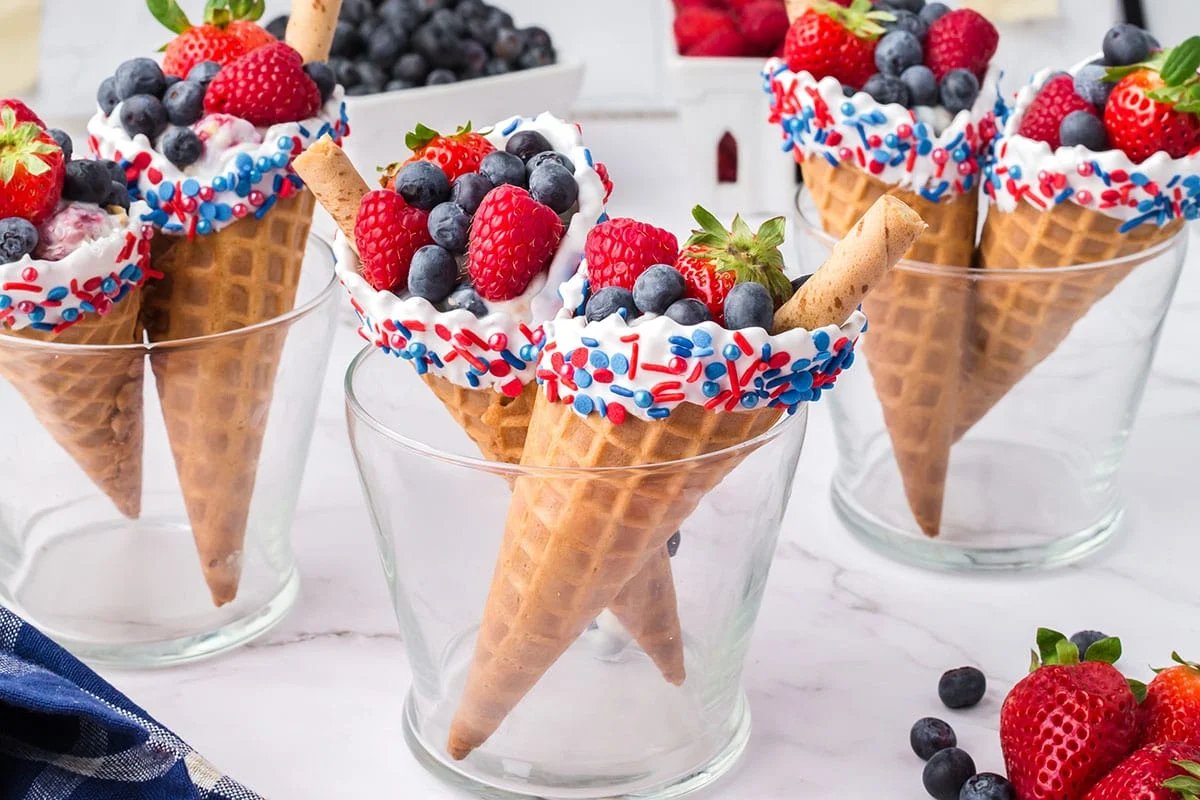 Waffle cones filled with fresh strawberries, raspberries, and blueberries, topped with white icing and red, white, and blue sprinkles make the perfect patriotic desserts when placed in clear glass cups.