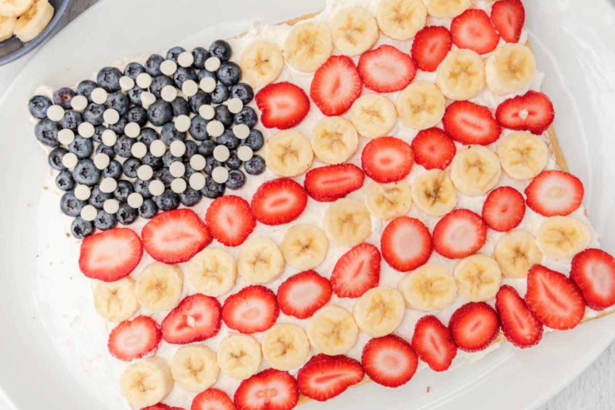A patriotic dessert arranged to resemble the American flag using blueberries and white candies for the stars, with strawberry and banana slices representing the stripes.