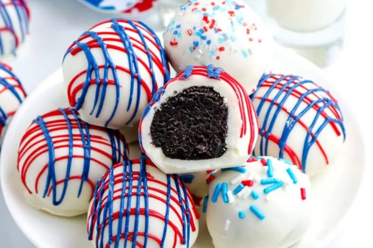 A plate of white chocolate truffles with red and blue drizzle and sprinkles, one truffle cut in half showing a dark filling. These patriotic desserts are perfect for any festive celebration.