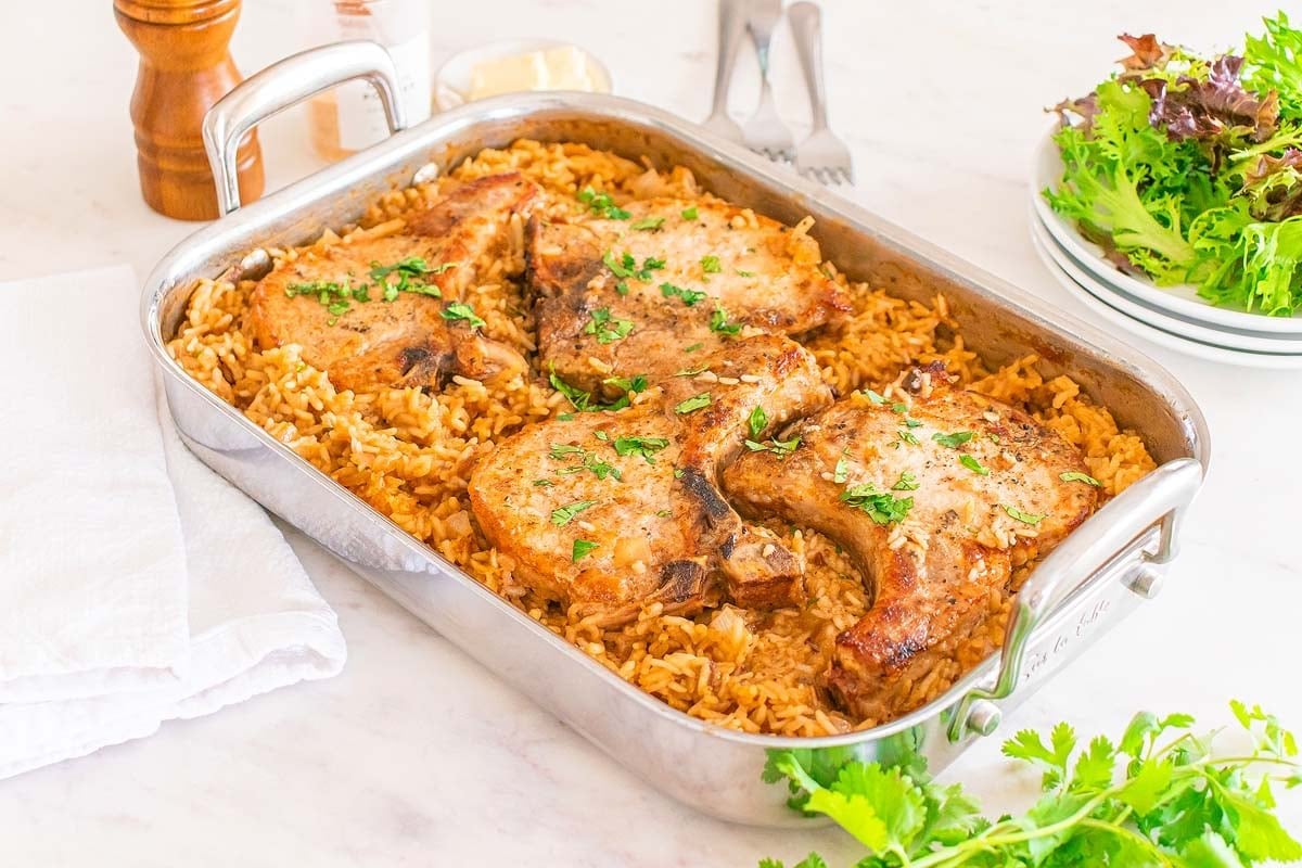Enjoy one of the best baked dinners with pork chops on a bed of seasoned rice in a rectangular pan, garnished with parsley.