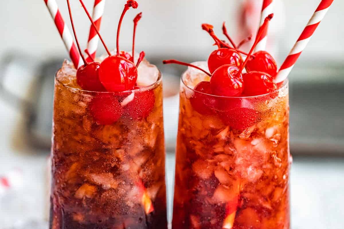 Two iced drinks in tall glasses are garnished with red maraschino cherries and striped red-and-white straws, embodying the best of cherry recipes.