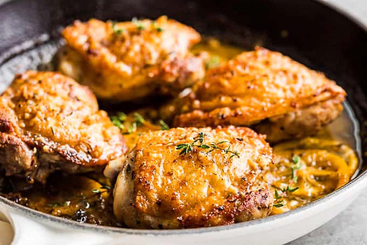 Pan-seared chicken thighs with crispy golden skin and sprigs of thyme in a skillet—one of the tastiest chicken thigh recipes you'll ever try.