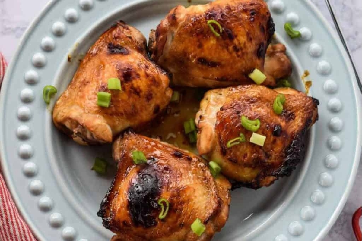 A plate of four grilled chicken thighs garnished with chopped green onions, perfect for those exploring new chicken thigh recipes.