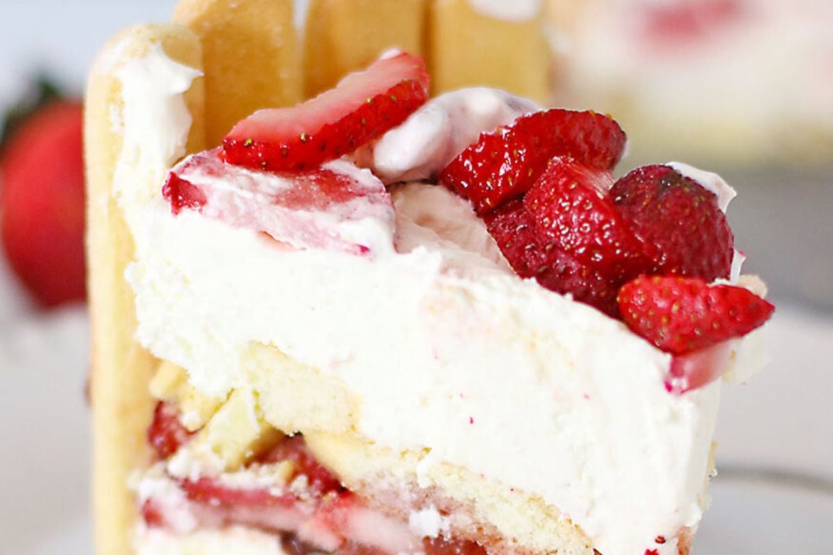 A slice of strawberry shortcake with layers of whipped cream, strawberries, and sponge cake on a white plate.