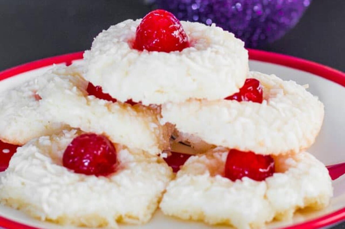 A plate of white cookies topped with shredded coconut and a red cherry in the center of each cookie, making it a delightful addition to any cherry recipes collection.