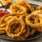 A plate of air fryer crispy onion rings served with ketchup and creamy sauce on a table.
