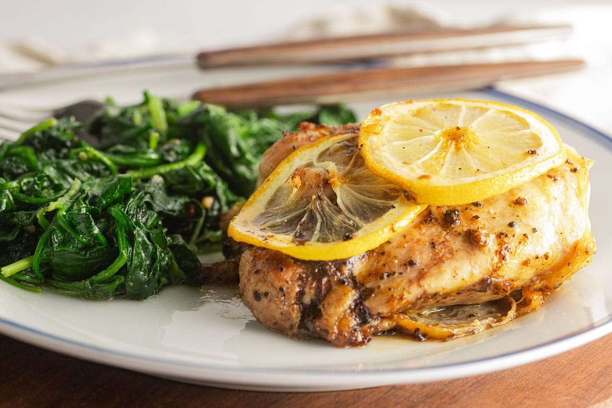 A plate of baked chicken breast topped with lemon slices, accompanied by a side of sautéed spinach, offers a delightful twist on traditional chicken thigh recipes.