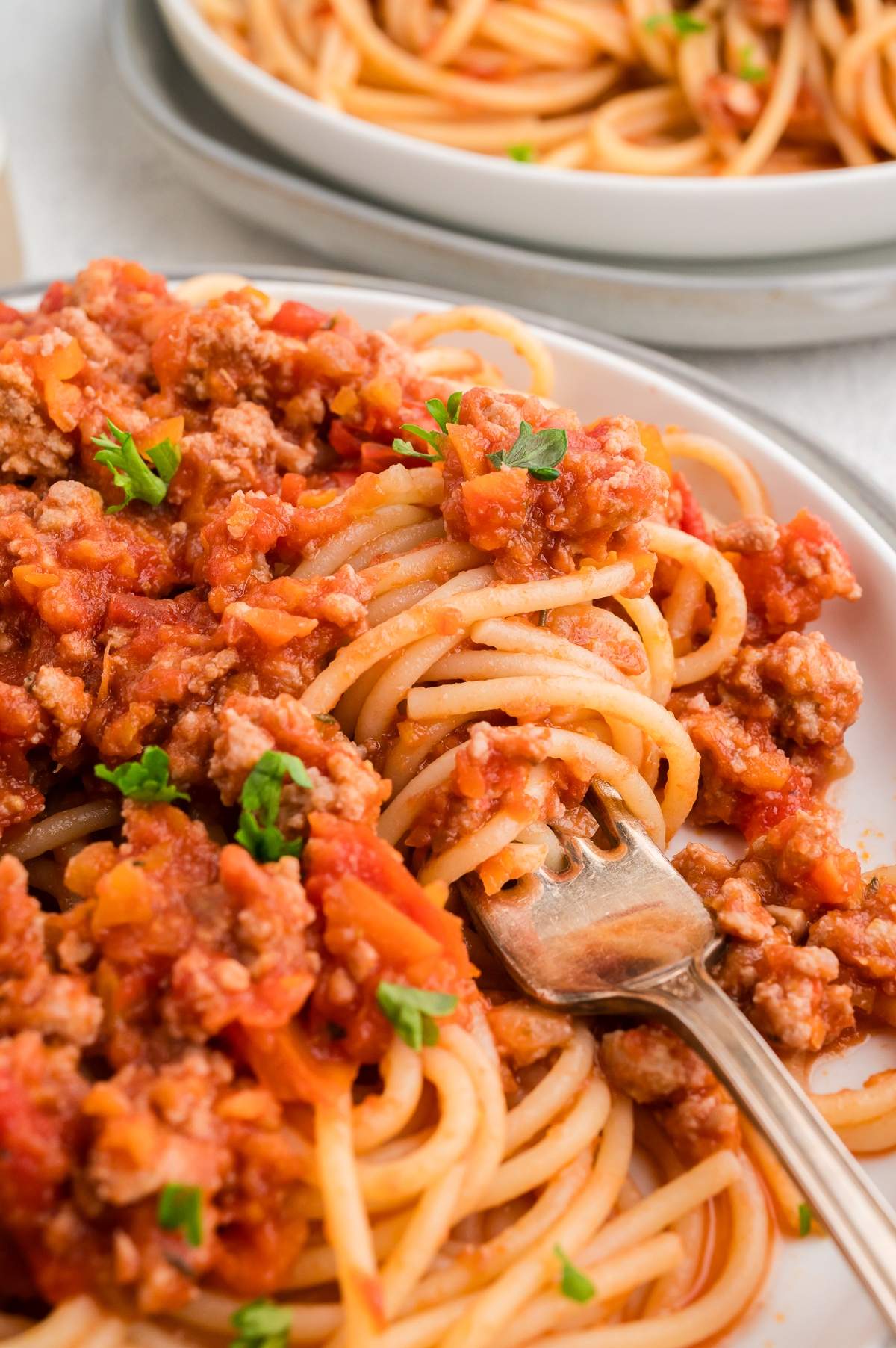 Close-up of spaghetti with savory chicken Bolognese sauce, garnished with parsley, and a fork twirling pasta on a white plate.