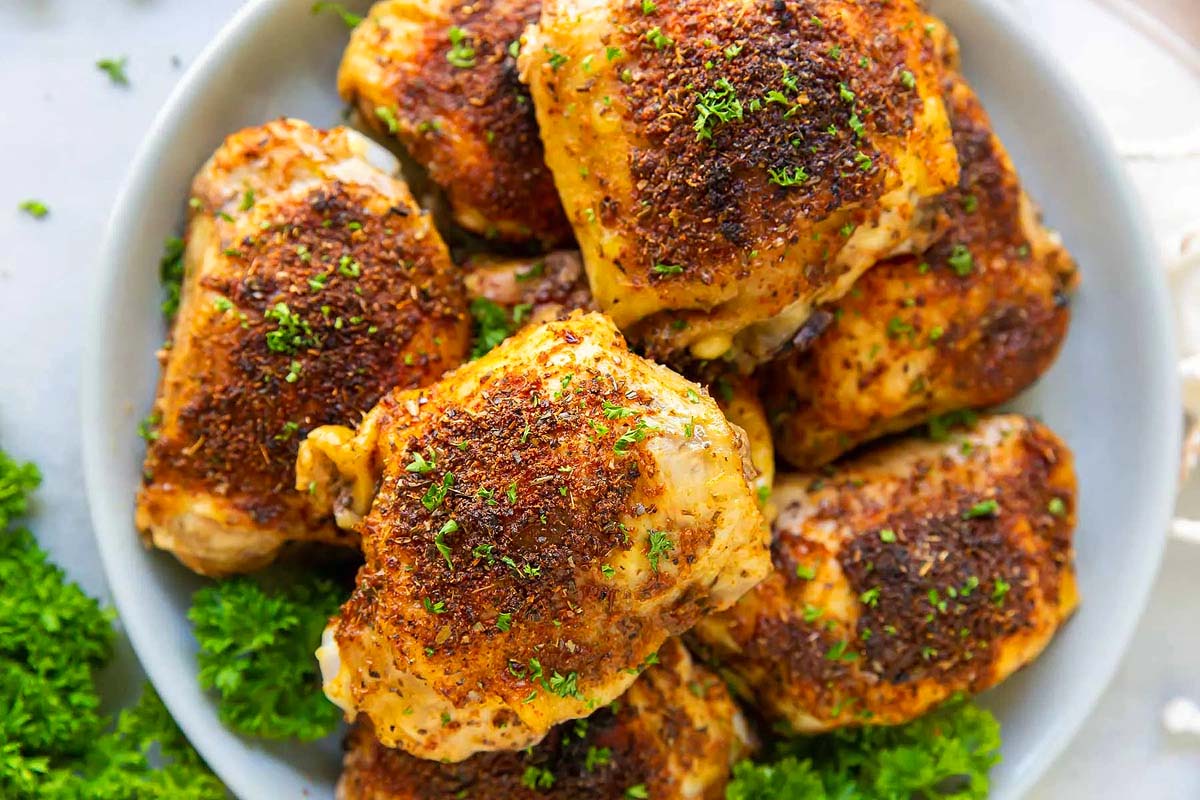 A plate of succulent grilled chicken thighs, celebrated in many chicken thigh recipes, is garnished with vibrant parsley and positioned beside fresh sprigs for an enticing presentation.