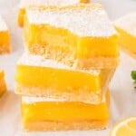 Stack of gluten-free lemon bars dusted with powdered sugar on a white surface, garnished with lemon slices and mint leaves.