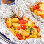 Gnocchi foil packets containing seasoned corn, and cherry tomatoes garnished with herbs, served on a blue plate.