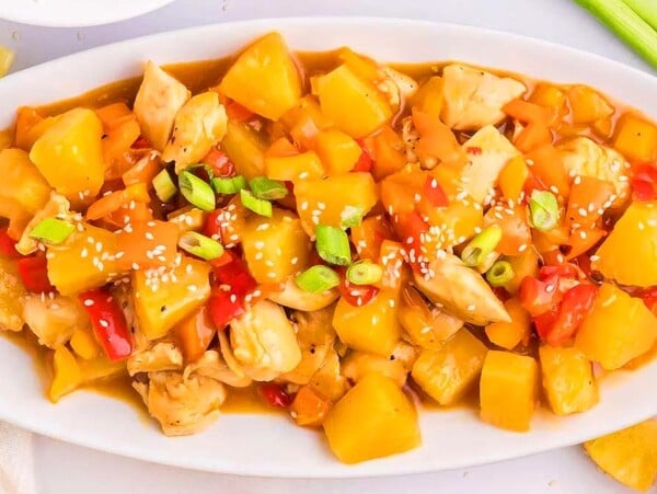 A plate of Hawaiian chicken with pineapple, bell peppers, and sesame seeds, garnished with green onions.