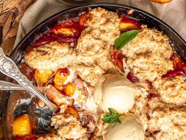 A skillet peach cobbler made with Bisquick mix, topped with two scoops of vanilla ice cream and a fresh mint sprig.
