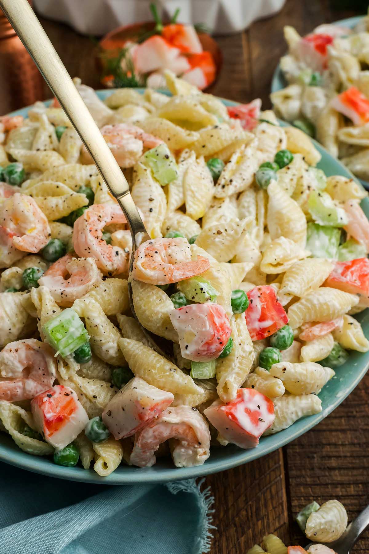 Pasta shells with shrimp, peas, and diced vegetables in a creamy sauce create a delicious seafood pasta salad, served in a blue bowl with a spoon.