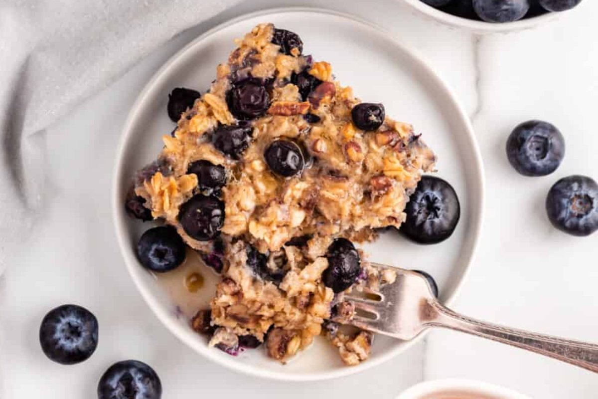 A slice of blueberry oatmeal bake on a white plate with a fork. Blueberries are scattered around the plate, showcasing one of the best blueberry recipes.