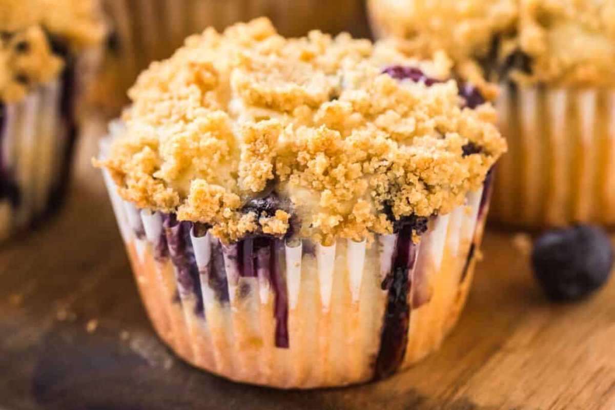 Close-up of a blueberry muffin with a crumbly streusel topping on a wooden surface. Blueberries are visible within the muffin, making it one of the most delightful blueberry recipes.