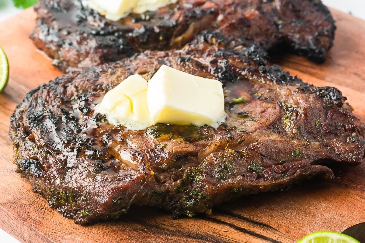 Grilled steaks topped with butter on a wooden cutting board, a simple yet delicious addition to your favorite steak recipes.