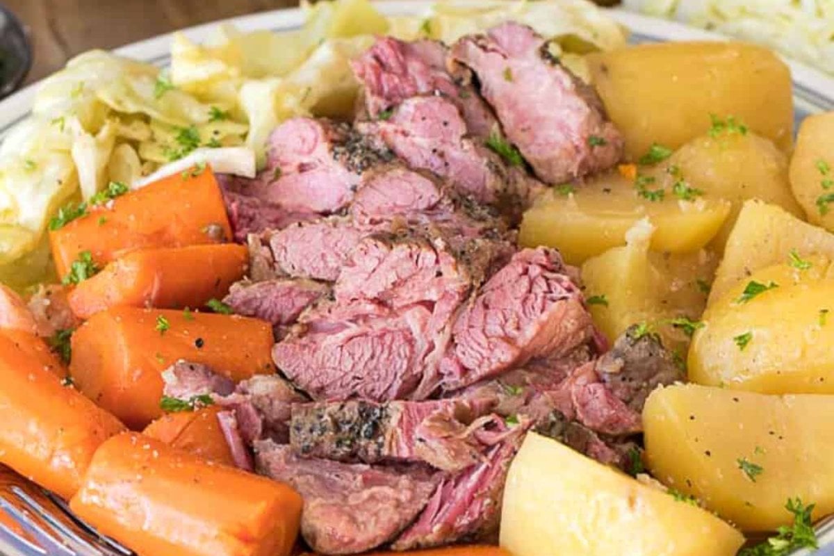 Plate of corned beef and cabbage with sliced carrots and potatoes, garnished with chopped parsley&mdash;a perfect example of slow cooker dinners.