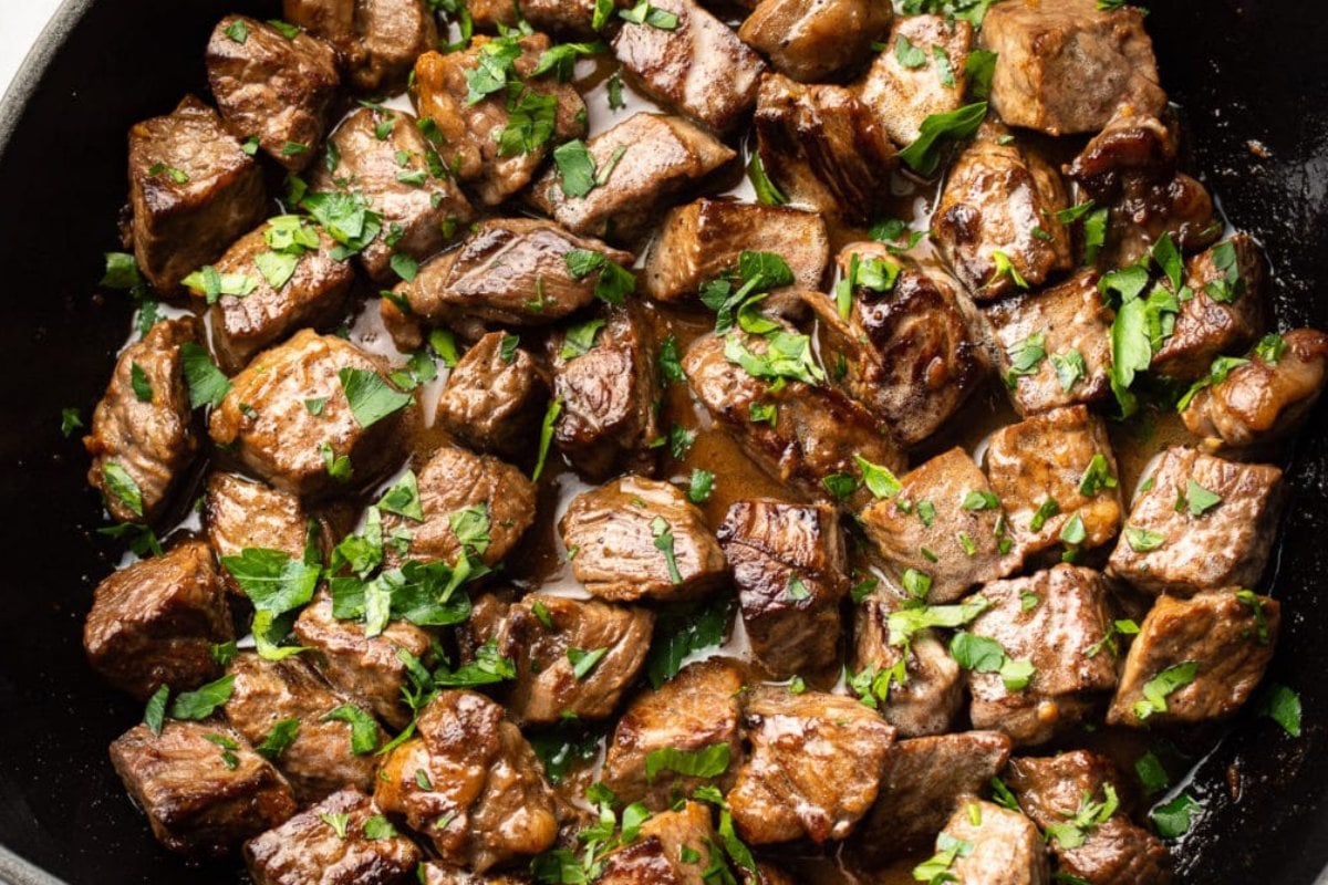 Close-up of cooked beef cubes, a highlight in many steak recipes, garnished with chopped parsley in a skillet.