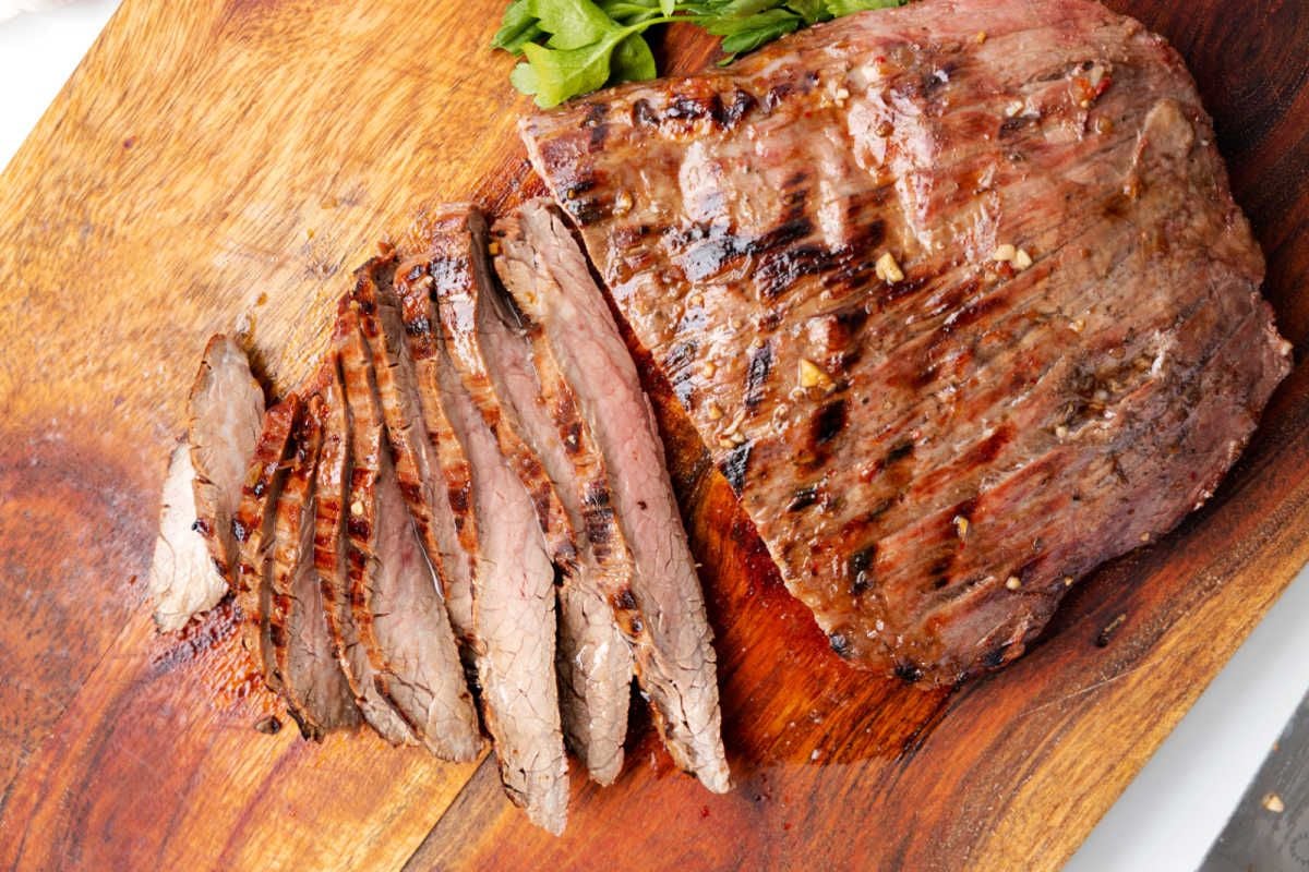 A grilled steak, partially sliced on a wooden cutting board, with green garnish visible on the side, perfect for those seeking delicious steak recipes.