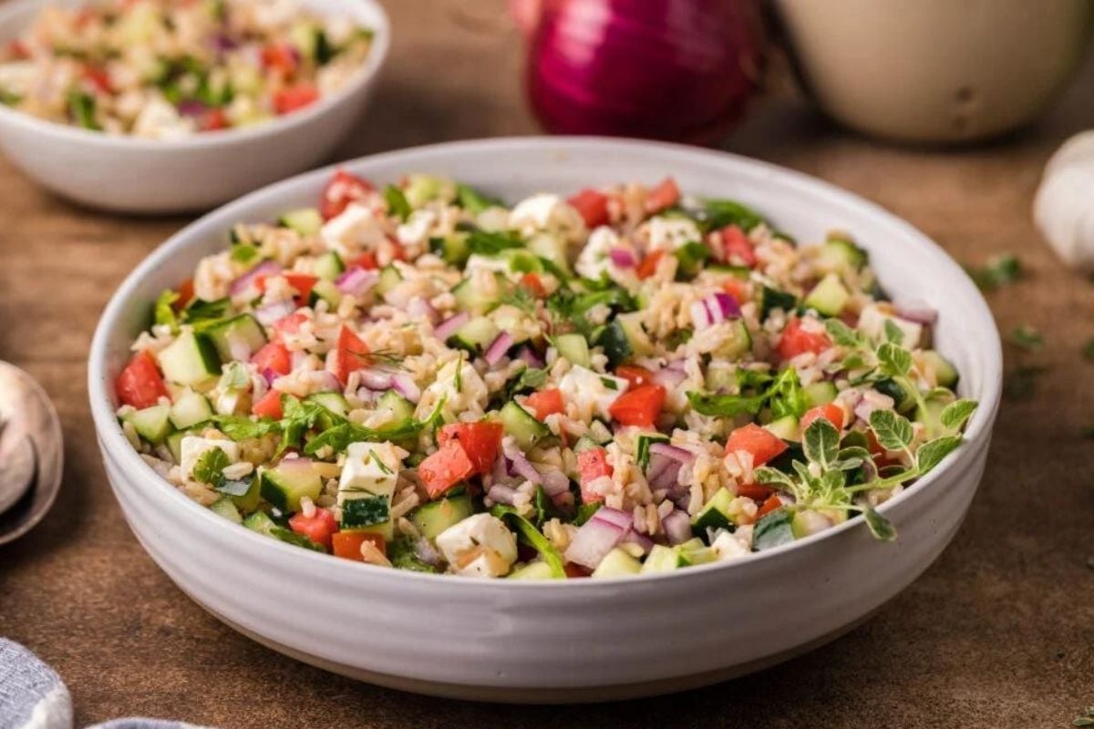 A bowl of fresh vegetable salad containing diced cucumber, tomato, red onion, and herbs, mixed with rice.