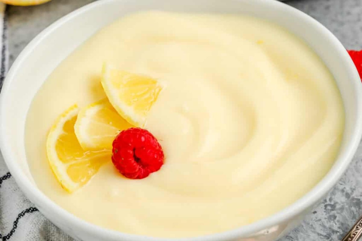 A bowl of creamy lemon pudding, one of the finest lemon desserts, adorned with three lemon slices and a single raspberry on top.