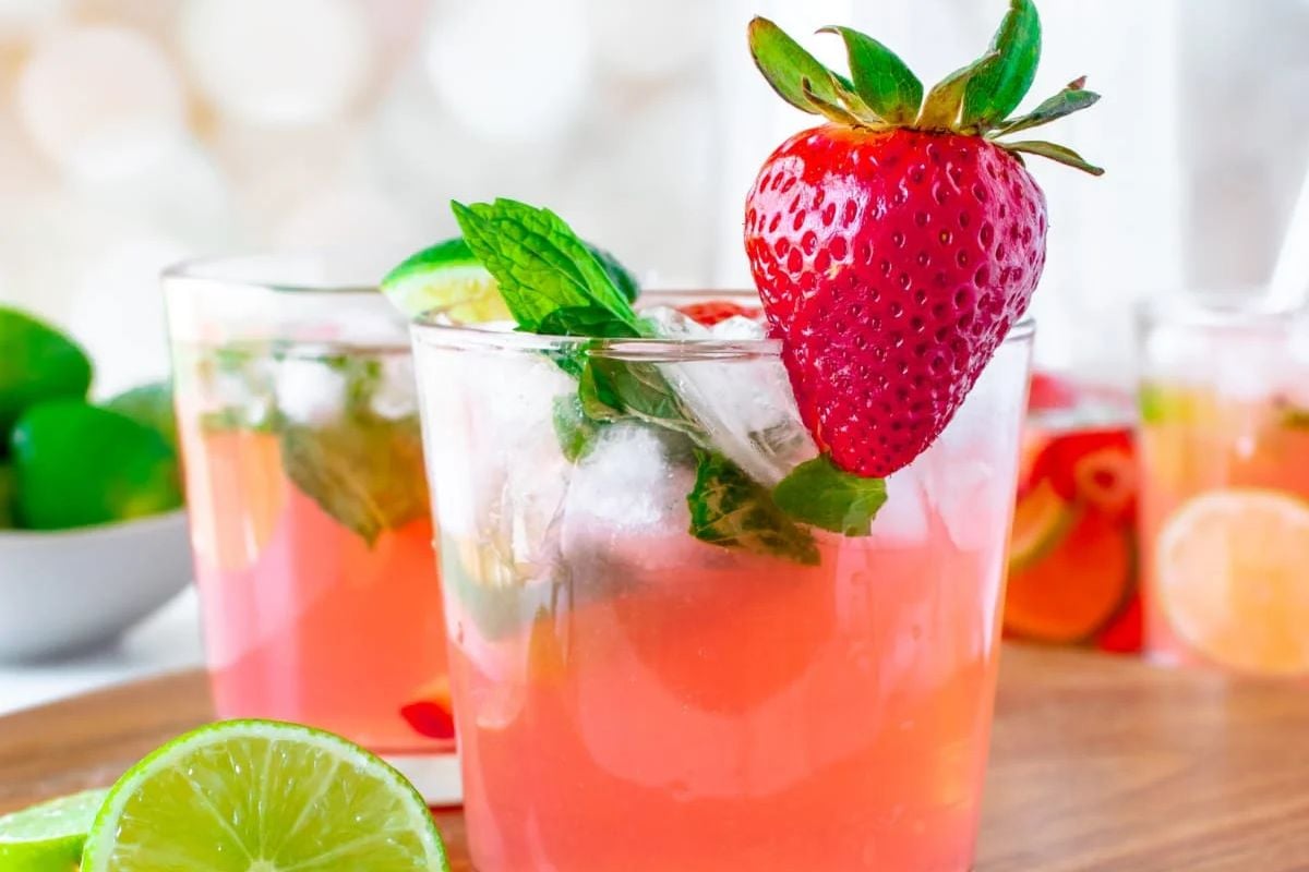 A glass of pink-colored beverage garnished with a strawberry, mint leaves, and lime slices, reminiscent of refreshing watermelon recipes.