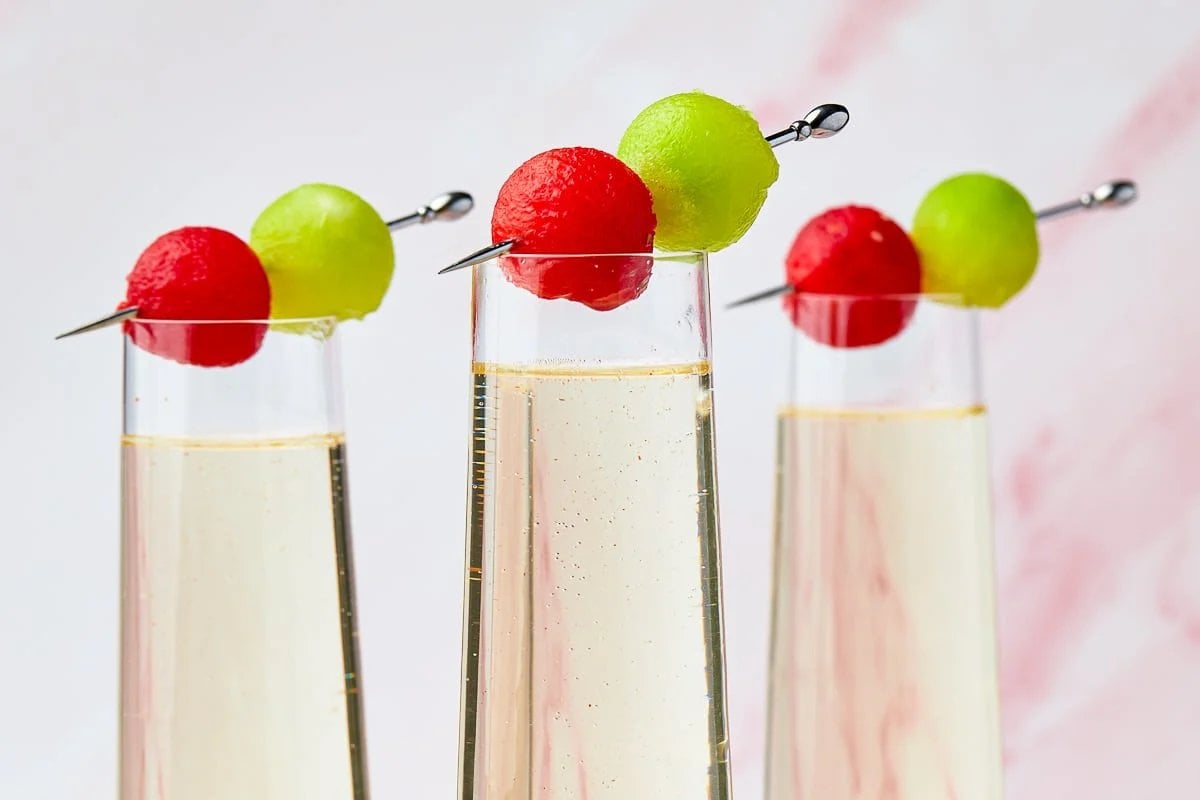 Three tall glasses filled with a light-colored beverage, each garnished with a red and green melon ball skewer—perfect for showcasing your favorite watermelon recipes.