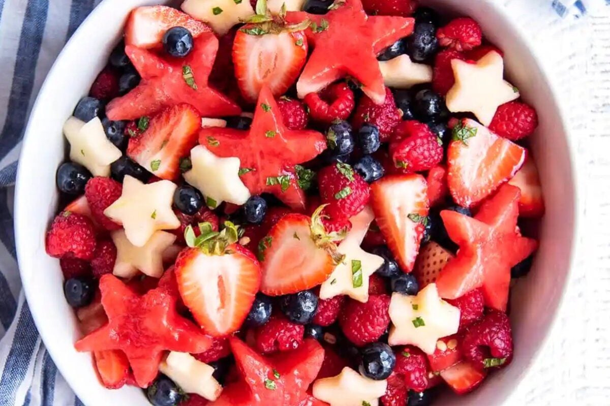 A bowl of mixed fruit, featuring star-shaped watermelon and pineapple pieces, strawberries, blueberries, and raspberries, garnished with a sprinkle of mint. Perfect for those exploring inventive watermelon recipes!