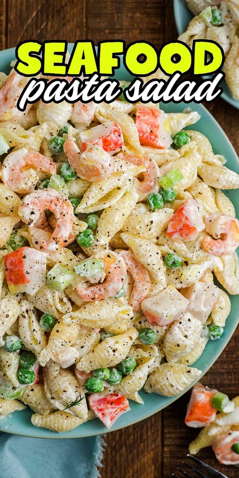 A bowl of seafood pasta salad with peas, shrimp, imitation crab, and shells, topped with black pepper.