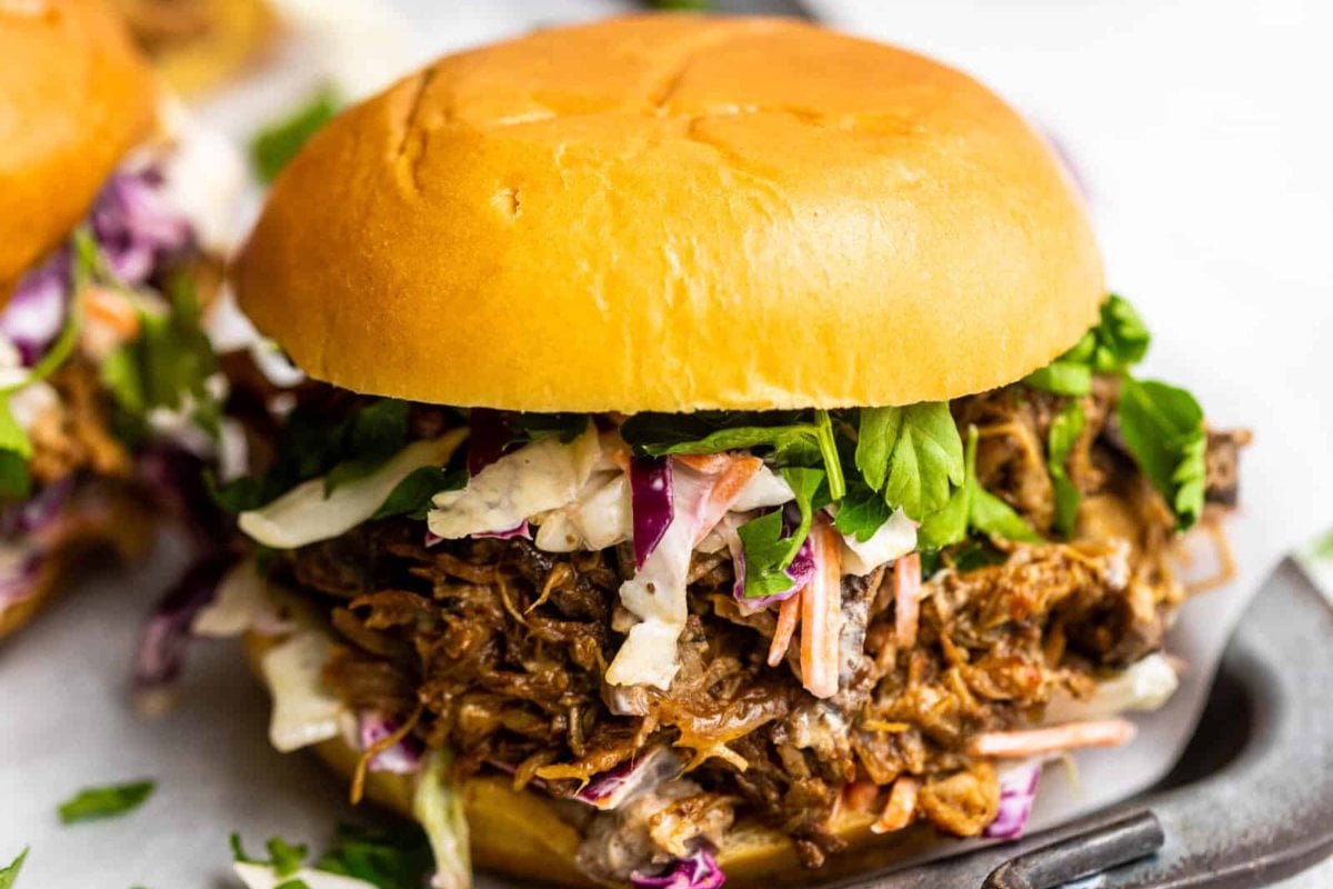 Close-up of a delicious pulled pork sandwich, perfected from slow cooker dinners, topped with coleslaw and fresh greens in a bun.