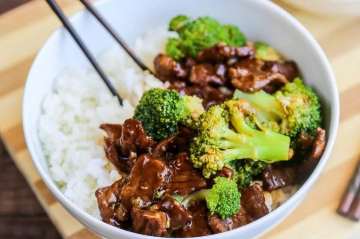 A bowl of white rice topped with broccoli and slices of beef in a savory brown sauce, perfect for those who appreciate slow cooker dinners, with black chopsticks placed on the side.