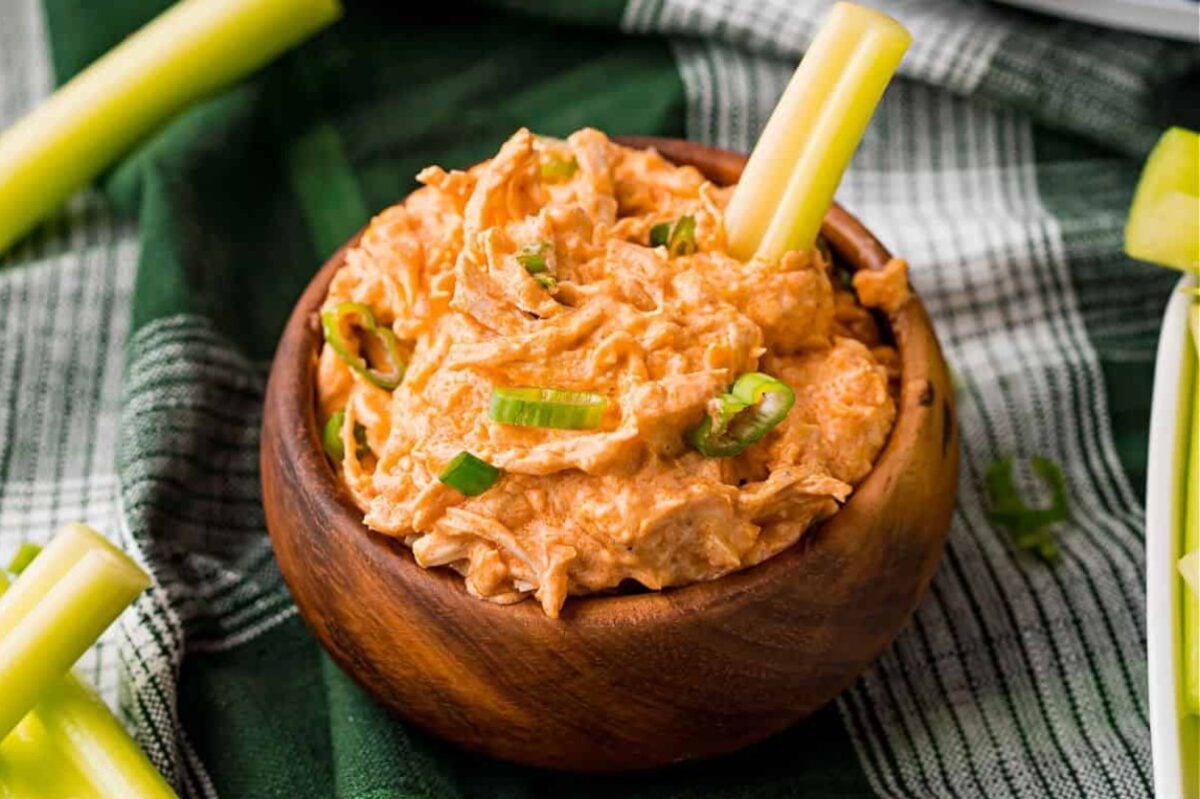 Buffalo chicken dip in a wooden bowl, garnished with green onions and served with celery sticks for dipping—a perfect addition to your collection of easy slow cooker dinners.