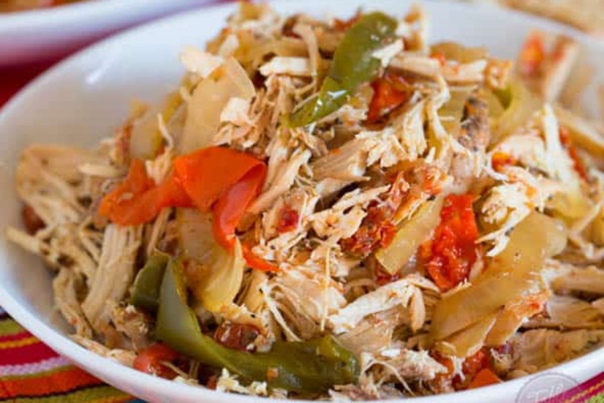 A delightful slow cooker dinner with shredded chicken mixed with colorful bell peppers, onions, and tomatoes, served in a white bowl.
