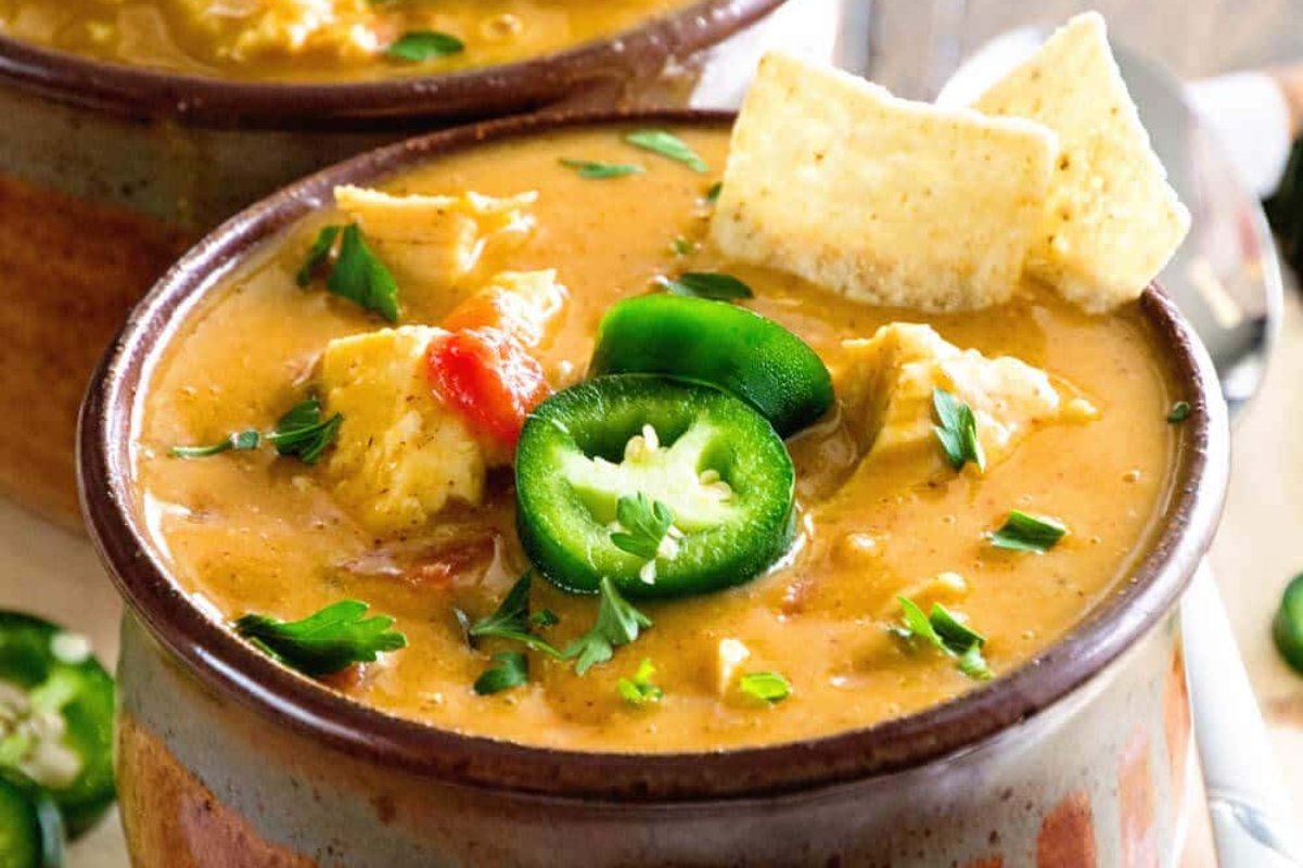 A bowl of creamy soup, perfect for slow cooker dinners, garnished with jalape&ntilde;o slices, tortilla chips, and fresh herbs.
